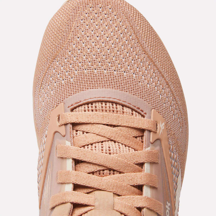 Close-up of Reebok Women's Nano X4 Training Shoes in peach, highlighting their lightweight mesh upper, laces, part of the tongue with visible stitching, and breathable texture details.
