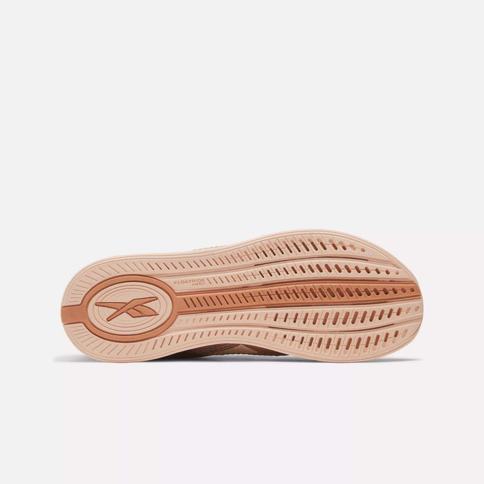 The image shows the outsole of the Reebok Women's Nano X4 Training Shoes, featuring a light brown rubber sole with textured grooves and an oval Reebok logo near the heel—ideal for lightweight training.