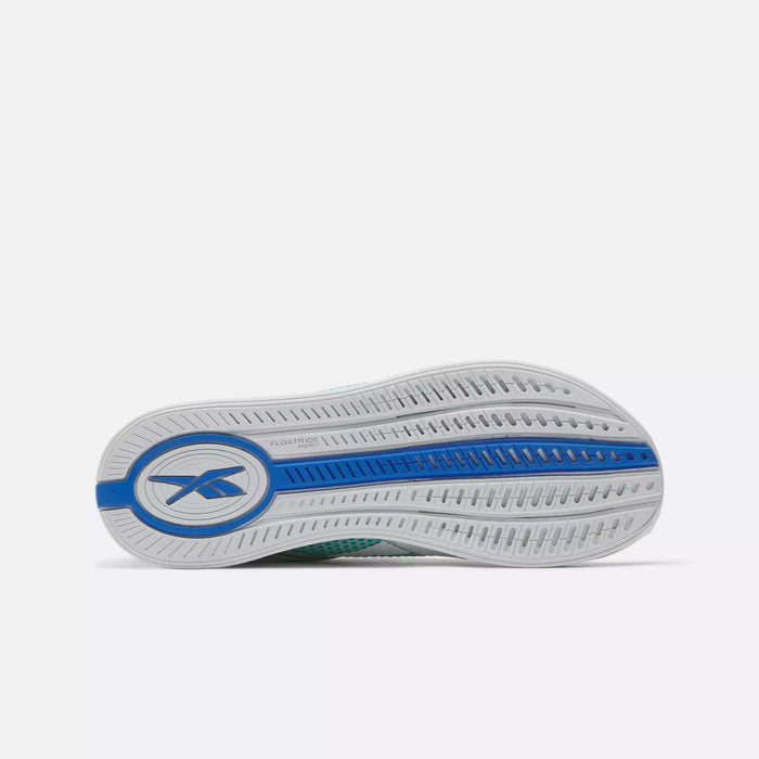 The image displays the sole of Reebok Women's Nano X4 Training Shoes, featuring a mostly white base with blue accents and the Reebok logo by the heel. The lightweight sole has textured grooves for traction and a curved design.