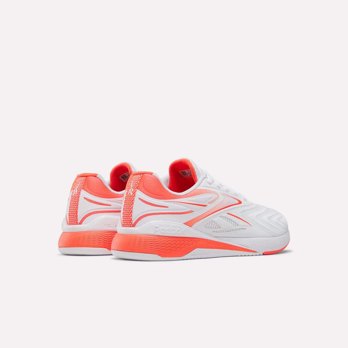 The Reebok Women's Nano X5 Edge Training Shoes in white feature bright red-orange accents on the sides, heel, and sole. Displayed against a plain white background, the shoes are angled to show their side and back views.