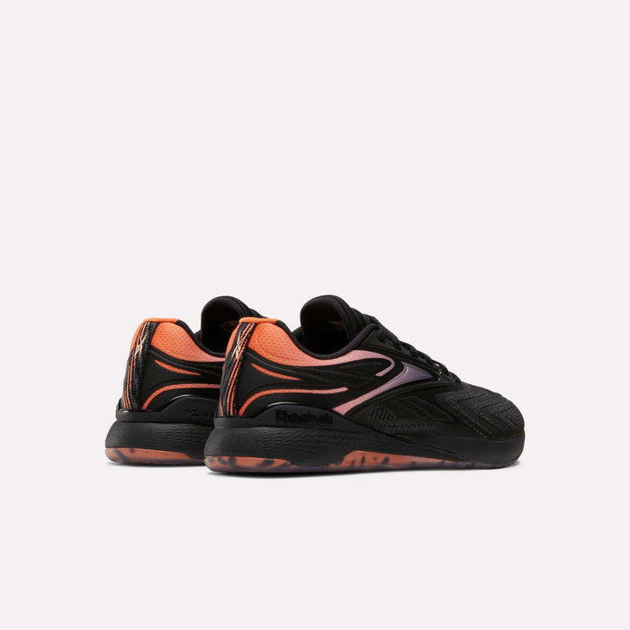 The image shows the Reebok Women's Nano X5 Edge Training Shoes in black with orange and pink accents, featuring a wavy side design and a patterned orange and black sole, viewed from the rear against a plain light background.