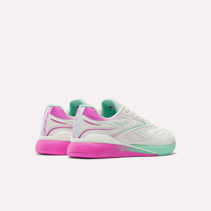 The Reebok Women's Nano X5 Edge Training Shoes feature a white upper with vibrant purple and mint green accents, plus a gradient sole fading from pink to green—shown from the back and side against a plain white background. Perfect for HIIT classes.
