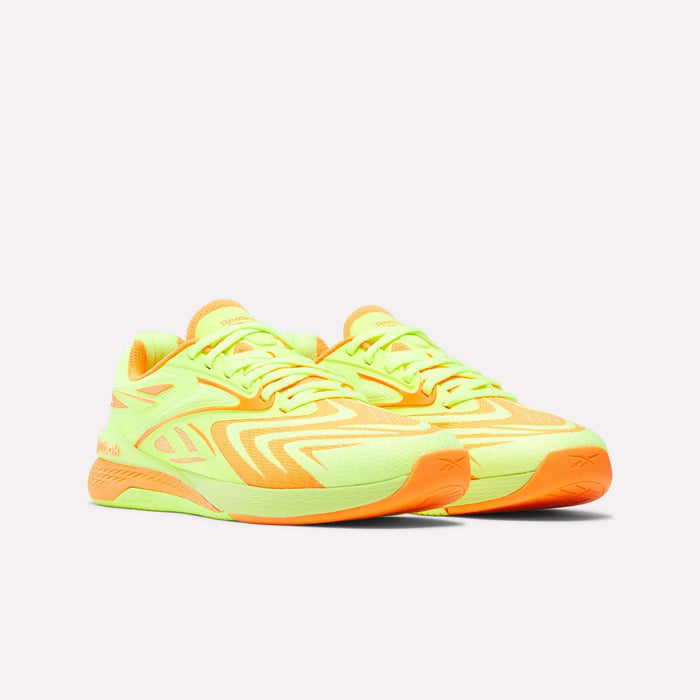The Reebok Women's Nano X5 Edge Training Shoes in neon yellow and orange feature a bold, angular pattern and thick soles—ideal for HIIT classes—shown on a plain white background.