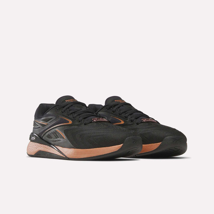 The Women's Nano X5 Edge Training Shoes from Reebok feature black uppers with copper accents and soles. Displayed on a white background, they’re perfect for your next HIIT class.