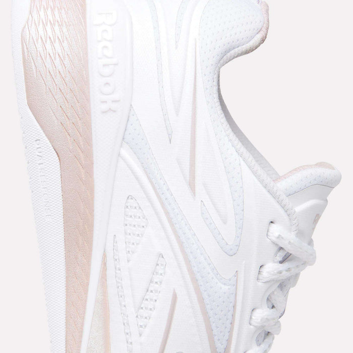 Close-up of the Reebok Women's Nano X5 Edge Training Shoes in white with light pink accents, featuring side logo, textured midsole, and partial laces set against a light background.