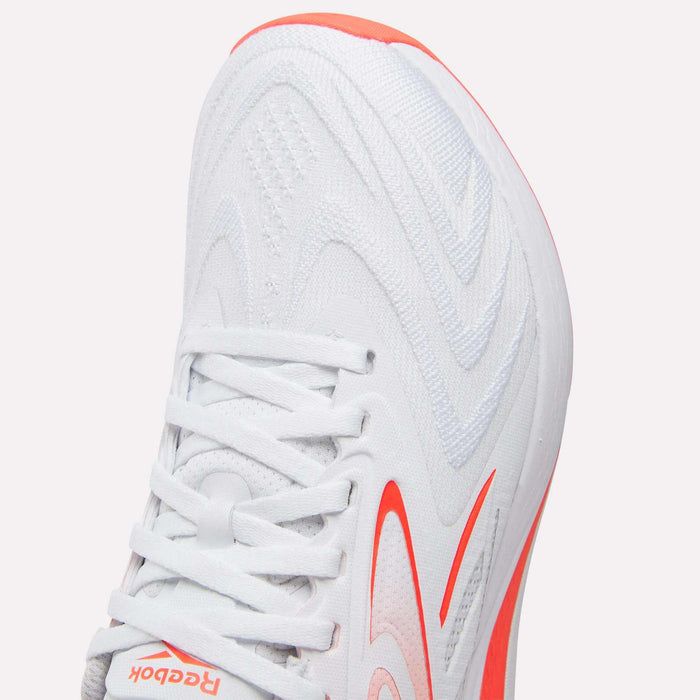 Close-up of the Reebok Women's Nano X5 Edge Training Shoes in white with orange accents, showcasing a wavy-patterned upper, white laces, and a partially visible logo near the toe. Perfect addition to any women’s HIIT shoe collection.