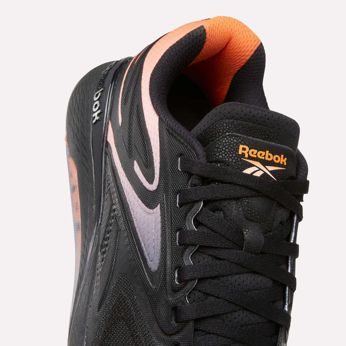 Close-up of the Reebok Women's Nano X5 Edge Training Shoes in black with orange and light purple accents, black laces, orange Reebok logos on tongue and side, and an orange inner lining.
