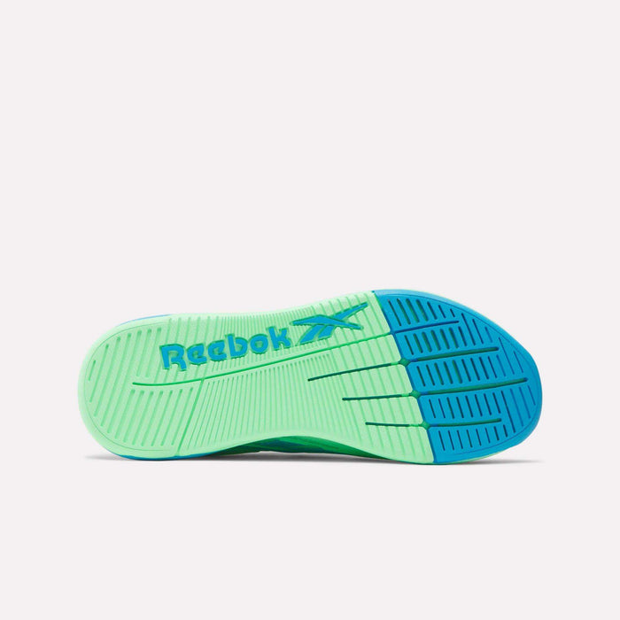 The image displays the sole of Reebok Women's Nano X5 Edge Training Shoes, with a light green base, blue toe area, and "Reebok" in blue. Grooved patterns provide traction for HIIT classes and workouts.