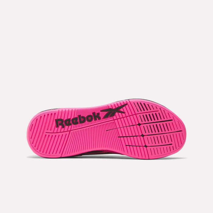 The image displays the bottom view of a bright pink Reebok Women's Nano X5 Edge Training Shoe sole with black Reebok branding and grip patterns, ideal for HIIT classes, set against a plain light background.