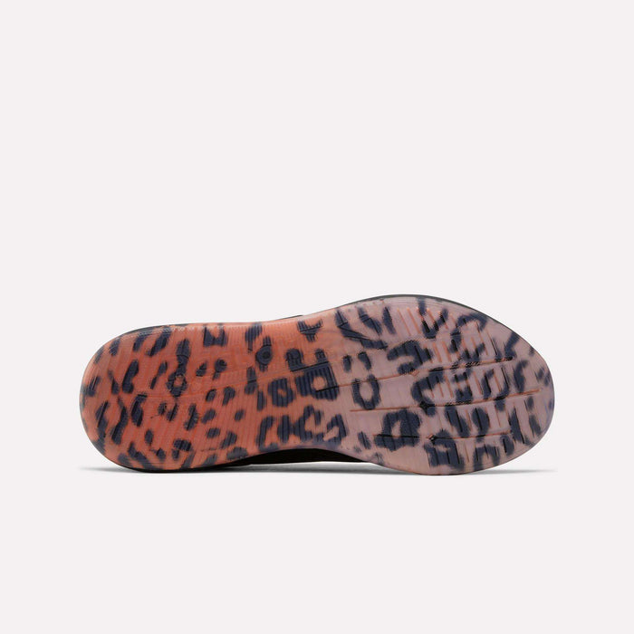 The image displays the sole of the Reebok Women's Nano X5 Edge Training Shoes, featuring a translucent base with an eye-catching orange, black, and brown leopard print pattern covering the entire bottom.