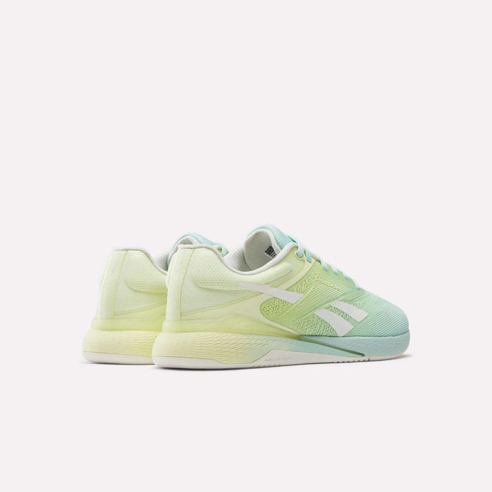 The Reebok Women's Nano X5 Training Shoes in pastel green and yellow feature white soles and signature stripes, shown from an angled rear view on a plain white background.