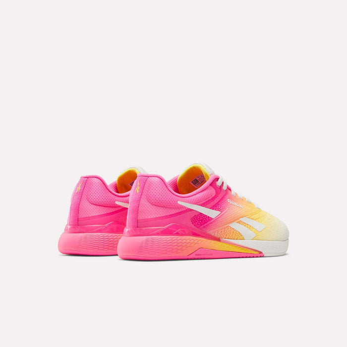 The Reebok Women's Nano X5 Training Shoes feature a gradient design in bright pink, yellow, and orange with white soles and logos, displayed from a rear side angle against a plain white background.