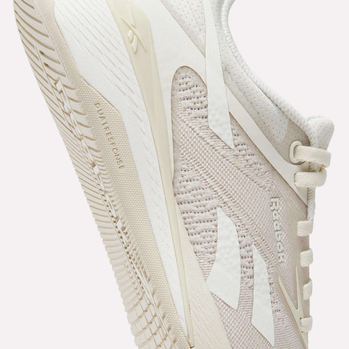 A close-up of Reebok Women's Nano X5 Training Shoes in light beige, highlighting the side mesh texture, Reebok logo, and detailed sole featuring the "DUAL DENSITY" text.