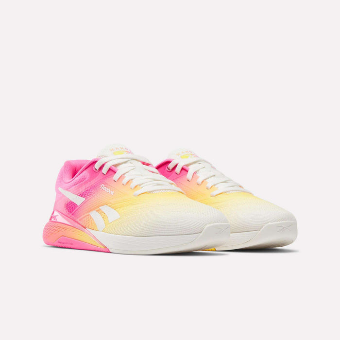 The Reebok Women's Nano X5 Training Shoes feature a comfortable fit and a gradient design in white, yellow, and pink with white laces, white soles, and side Reebok logos, shown on a plain white background.