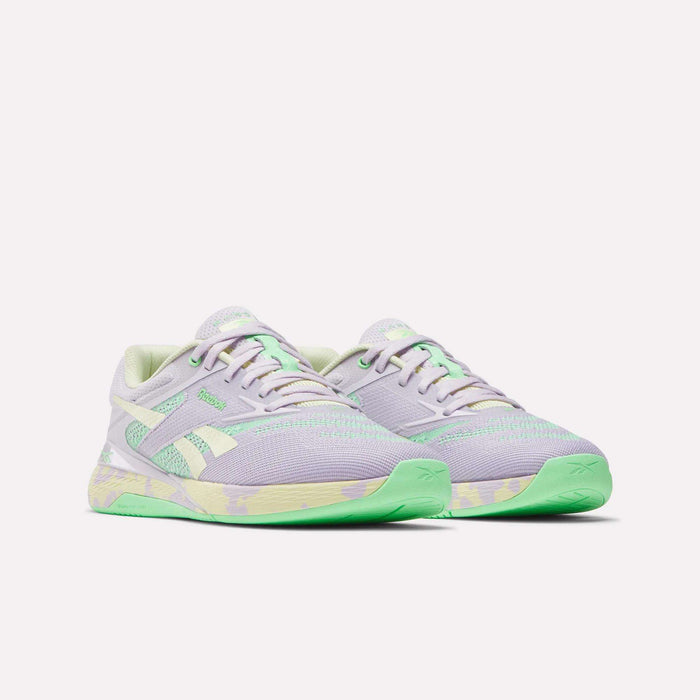 The Reebok Women's Nano X5 Training Shoes are pastel purple with light green accents and soles, plus white side stripes and a green-and-yellow midsole pattern. Comfortable running shoes displayed on a plain white background.