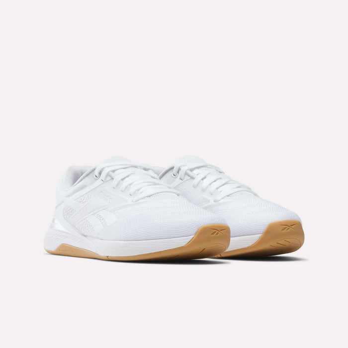 Displayed on a plain white background, the Reebok Women's Nano X5 Training Shoes feature a white textured upper, light brown rubber soles, and are designed for comfort.
