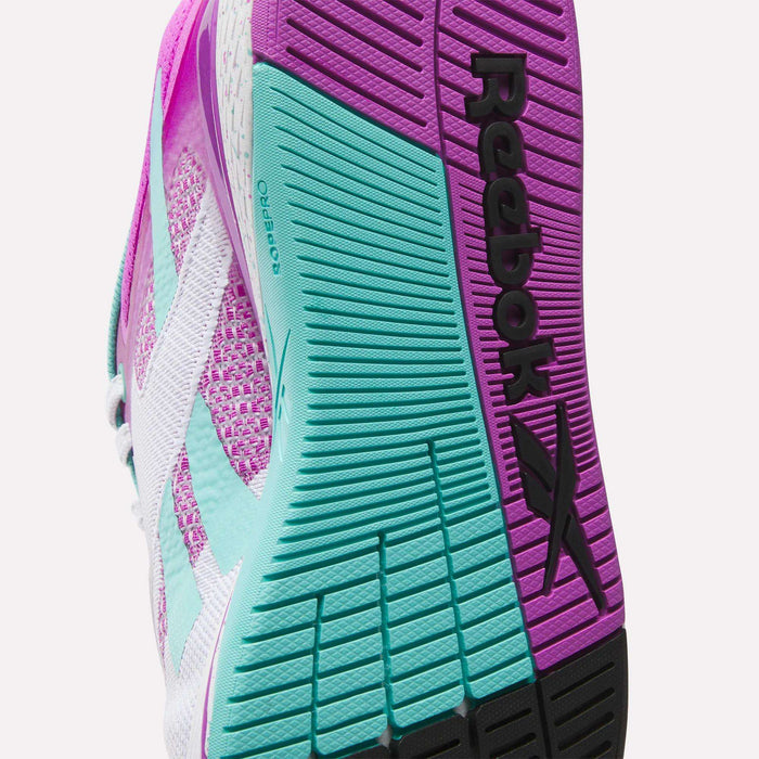 Close-up of the sole of Reebok Women's Nano X5 Training Shoes, showing textured grip patterns in pink, teal, and black, with the “Reebok” name and logo clearly visible.