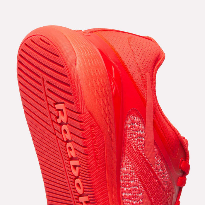 Close-up of Reebok Women's Nano X5 Training Shoes in bright red, featuring a textured sole with Reebok branding, mesh upper, and detailed stitching against a plain white background.