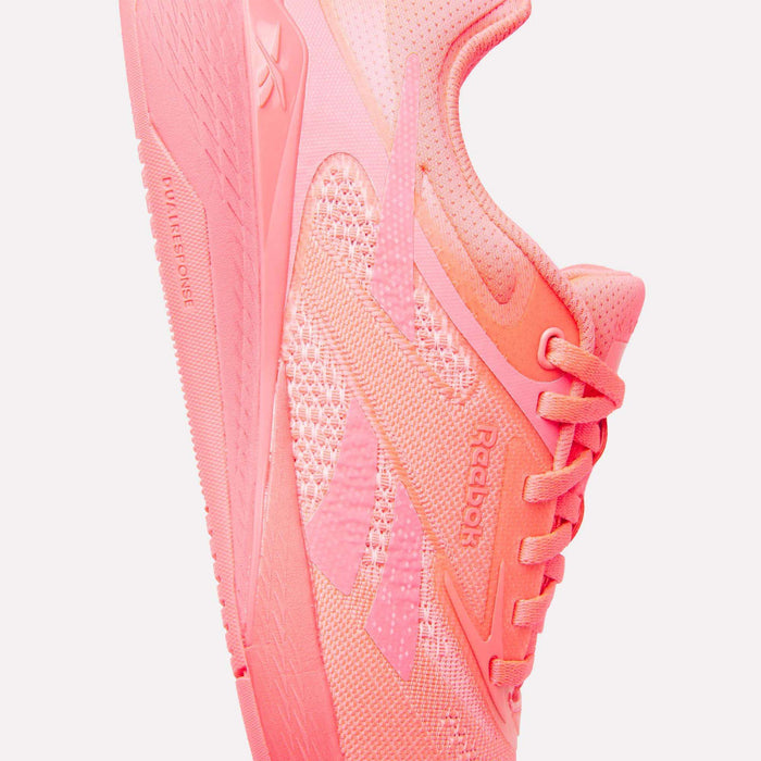 A close-up side view of the Reebok Women's Nano X5 Training Shoes in bright pink, highlighting the textured fabric, laces, and signature Reebok logo on this stylish women’s training shoe.