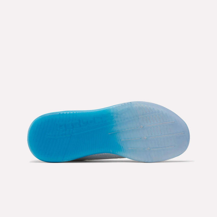 The image shows the sole of Reebok Women's Nano X5 Training Shoes, with a gradient from solid blue at the heel to translucent white at the toe, textured grip patterns, and a visible Reebok logo in the midfoot area.