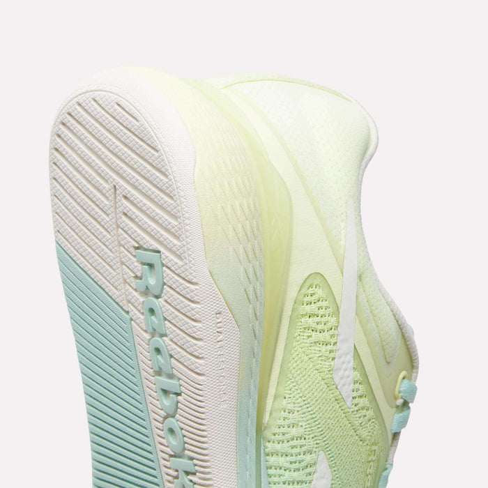 Close-up of the sole and side of a light green and white Reebok Women's Nano X5 Training Shoe, featuring textured tread, mesh fabric, and the Reebok logo on the bottom—engineered for comfort during women's training.