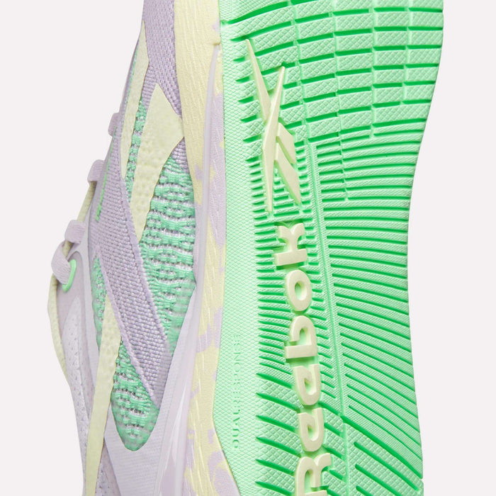 Close-up of Reebok Women's Nano X5 Training Shoes, iconic for training, with a light purple and mint green knit upper, textured mint green sole, and the Reebok logo in light yellow on the side and sole.