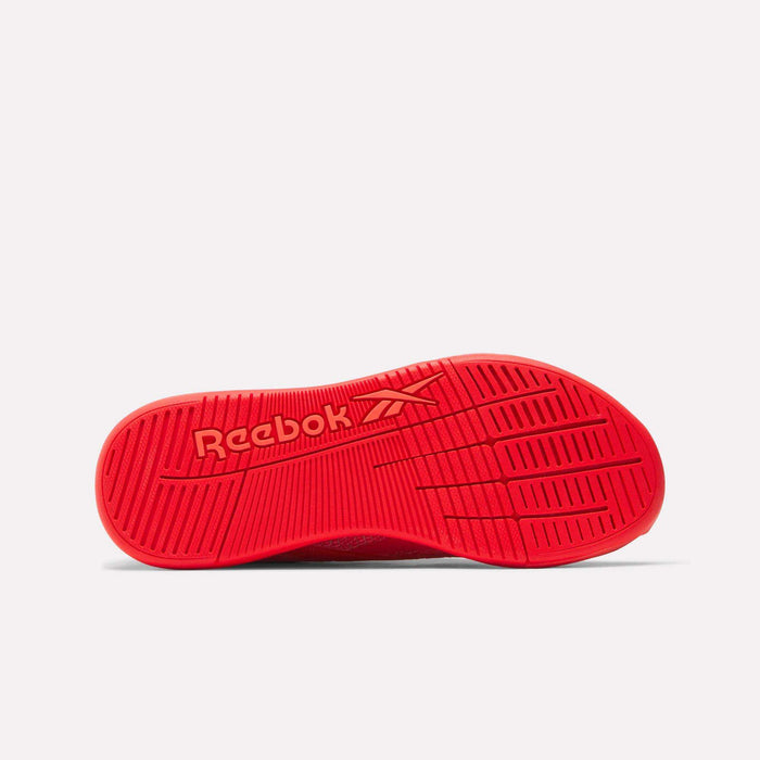 The image displays the sole of a Reebok Women's Nano X5 Training Shoe, featuring a red color, angled grooves for traction, and the Reebok logo. The shoe is shown with its sole facing up on a plain white background.