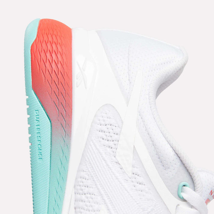 Close-up of Reebok Women's Nano X5 Training Shoes featuring a white, textured mesh upper for breathability and a comfy sole fading from turquoise at the heel to coral red at the back, with subtle branding on the side and heel.