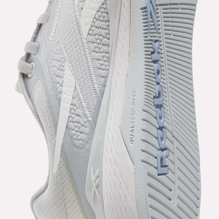 Close-up of two light grey Reebok Women's Nano X5 Training Shoes, highlighting the textured sole with the Reebok logo, breathable mesh upper, and sleek, comfortable design details.