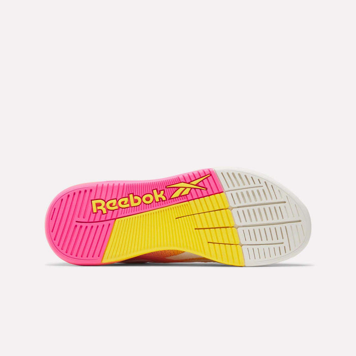 The image displays the sole of Reebok Women's Nano X5 Training Shoes, featuring pink, yellow, and white sections with a yellow Reebok logo on the pink area. The sole has textured patterns for grip.