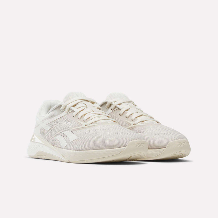 A pair of Reebok Women's Nano X5 Training Shoes in beige with white soles and mesh uppers, featuring a subtle side logo, displayed against a plain white background.