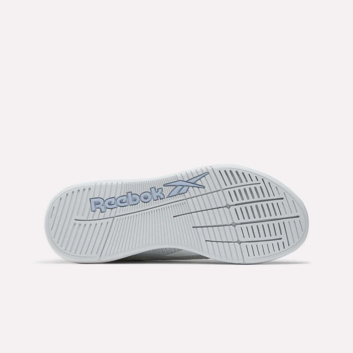 The image shows the white sole of Reebok Women's Nano X5 Training Shoes, with the blue Reebok logo and vector. The tread features linear and grid-like patterns for grip. The background is plain and light-colored.