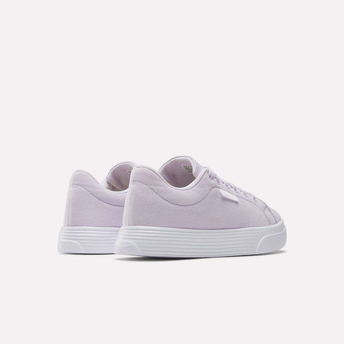 The Reebok Women's OnLux Court Lite Walking Shoes in light purple feature white soles and are shown from a rear side angle on a plain white background. These lightweight shoes offer comfort and style for walking.