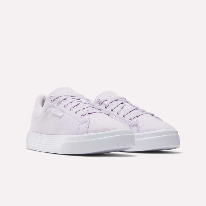 The Reebok Women's OnLux Court Lite Walking Shoes feature a light purple color, white soles, laces, and a minimalist design. Shown from the front on a plain white background, they're perfect for comfortable walks.