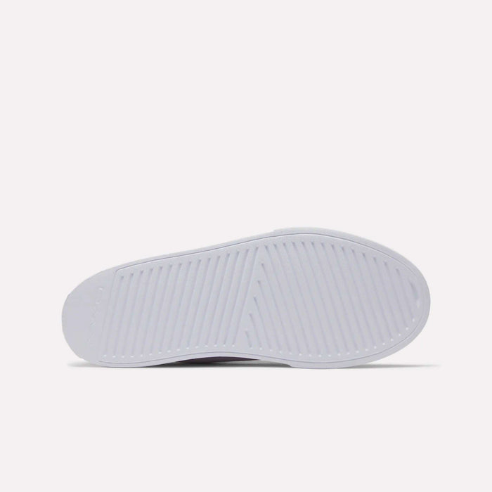 The image shows the sole of a white Women's OnLux Court Lite Walking Shoe by Reebok, viewed from the bottom. The sole has a textured pattern with diagonal and crosswise grooves for traction. The background is plain and light-colored.