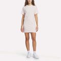 A woman wears a light pink Women's Oversized T-Shirt Dress and white Reebok sneakers with socks, standing against a plain white background.