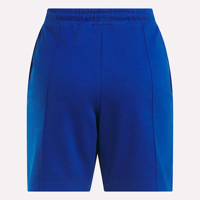 Reebok Women's Pintuck Long Shorts in bright blue feature an elastic waistband and side pockets. Made from soft cotton-blend fleece, these athletic shorts offer comfort and style for sports or everyday wear.