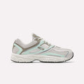 The Reebok Women's Premier Trinity Shoes are shown in a side profile, featuring gray and white colors with light aqua and taupe accents, mesh panels, and a black sole, blending retro tech style with modern design against a plain background.