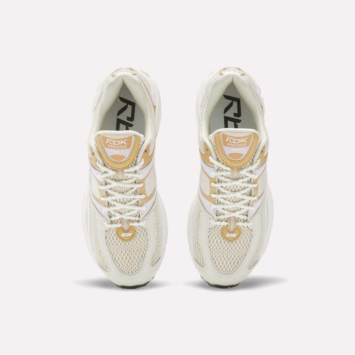 Top view of Women's Premier Trinity Shoes by Reebok in cream and beige, featuring white laces, mesh uppers, and branded tongues, inspired by retro tech running shoes, displayed on a white background.