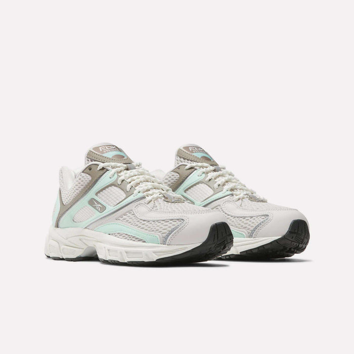 The Women's Premier Trinity Shoes by Reebok, shown in white and light mint green with mesh and suede panels, gray accents, and black rubber soles, offer a retro tech look against a plain white background.