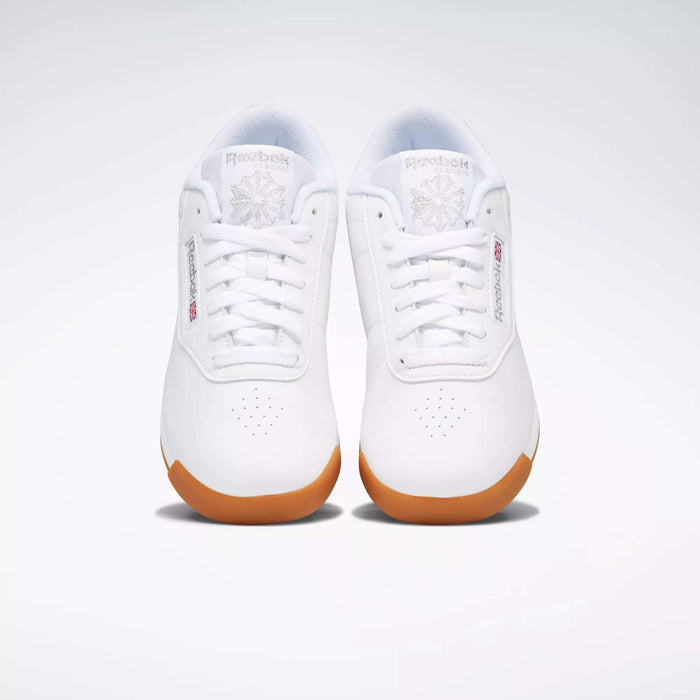 A pair of Reebok Women's Princess Shoes in white with gum soles, shown from above on a plain light background. These sneakers feature Reebok logos, toe perforations, and provide excellent cushioning for all-day comfort.
