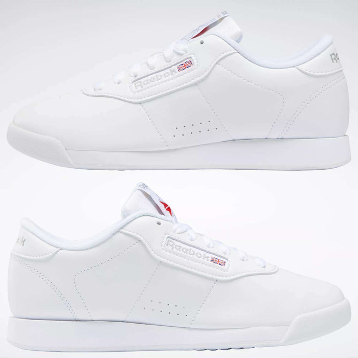 Two side views of Reebok Women's Princess Shoes in classic white, featuring cushioned soles, laces, subtle side branding, and heritage-inspired details like a small Union Jack flag next to the Reebok logo.
