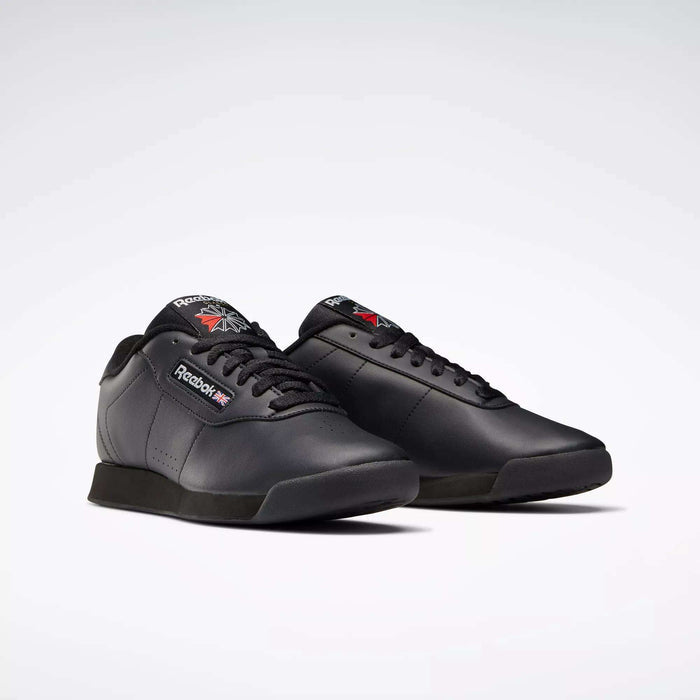 A pair of black Reebok Women's Princess Shoes displayed on a white background, with one shoe facing forward and the other slightly turned, highlighting their classic design and signature Reebok logo on the side and tongue.
