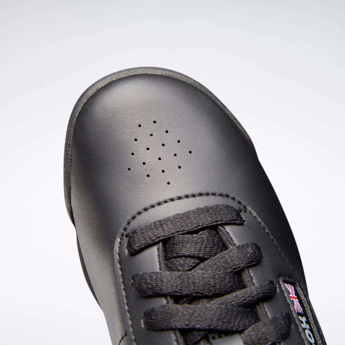 Close-up of the toe and laces on the Reebok Women's Princess Shoes in black leather, featuring small ventilation holes on the toe box, cushioned design, and a partial Reebok logo tag visible on the tongue.