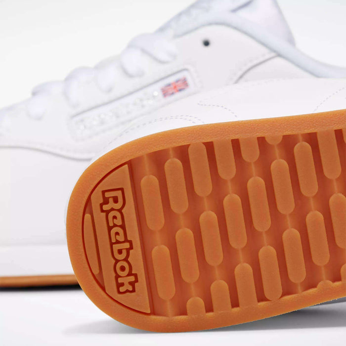 Close-up of Reebok Women's Princess Shoes, featuring an orange rubber sole with the embossed Reebok logo. A small Union Jack flag patch and part of the cushioned design are visible in the background.