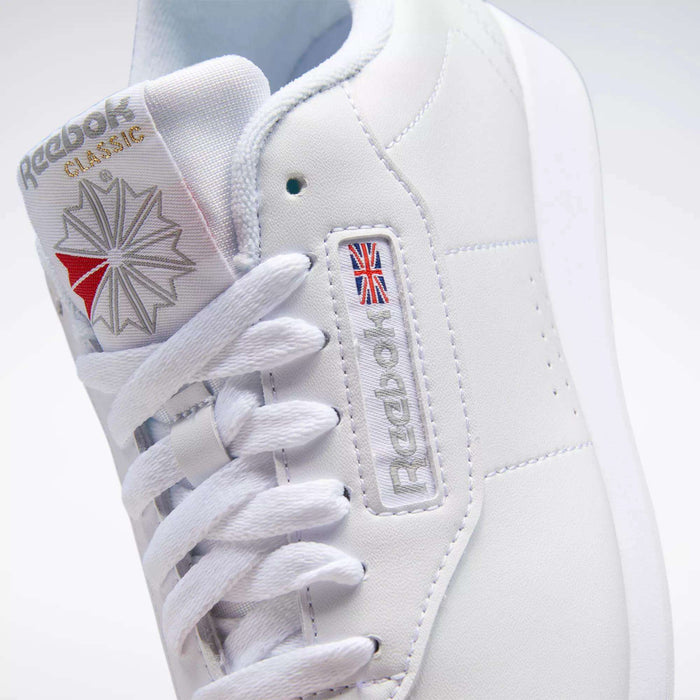 Close-up of a white Reebok Women's Princess Shoe featuring heritage style with the logo, Union Jack flag, white laces, and textured stitching details on the side and tongue.