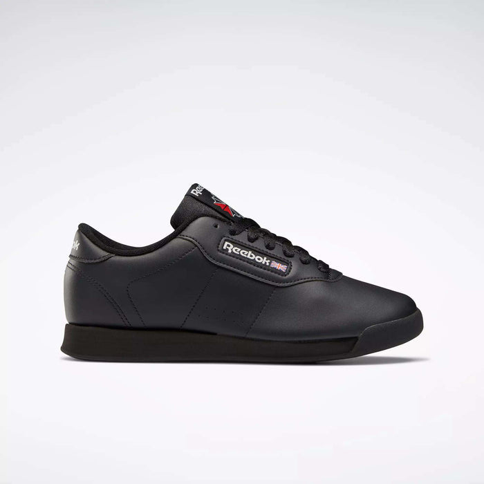 A pair of black Reebok Women's Princess Wide Shoes featuring a low-cut lace-up design, cushioned sole, and subtle Union Jack detail is shown against a plain light gray background.