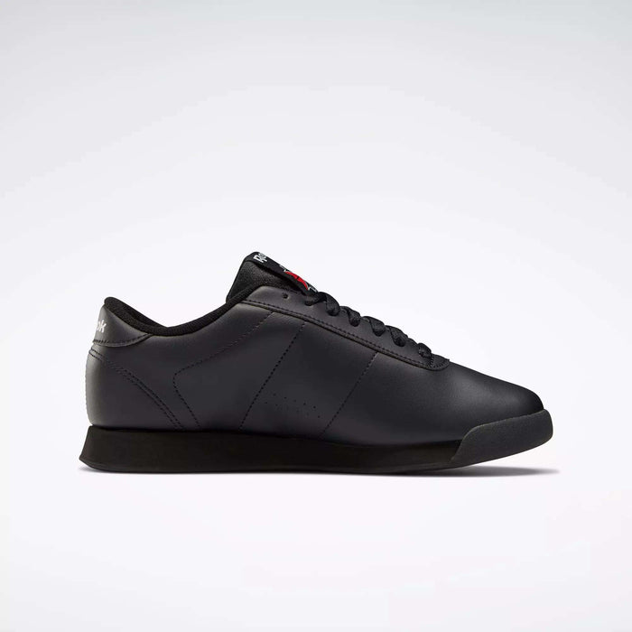 The Reebok Women's Princess Wide Shoes are classic black low-top sneakers with black laces and a subtle Union Jack logo on the heel, shown in side profile against a plain white background.