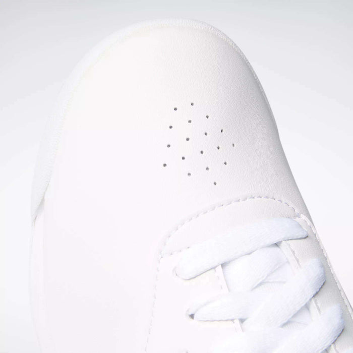 Close-up of Reebok Women's Princess Wide Shoes with small perforated holes and white laces at the toe. The plain, light background highlights the sneaker’s timeless Reebok style.