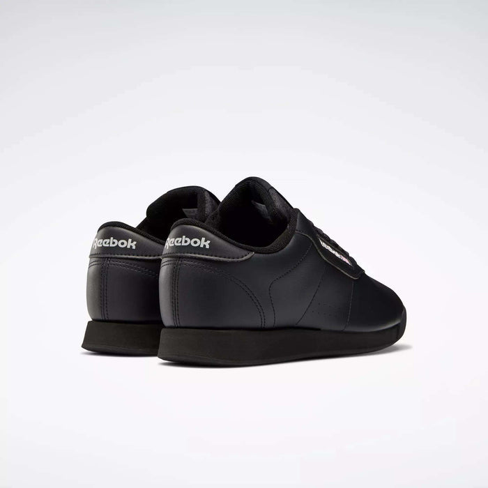 A pair of black Reebok Women's Princess Wide Shoes is displayed against a white background, shown from the back and side angles to highlight the Reebok branding on the heel and side.
